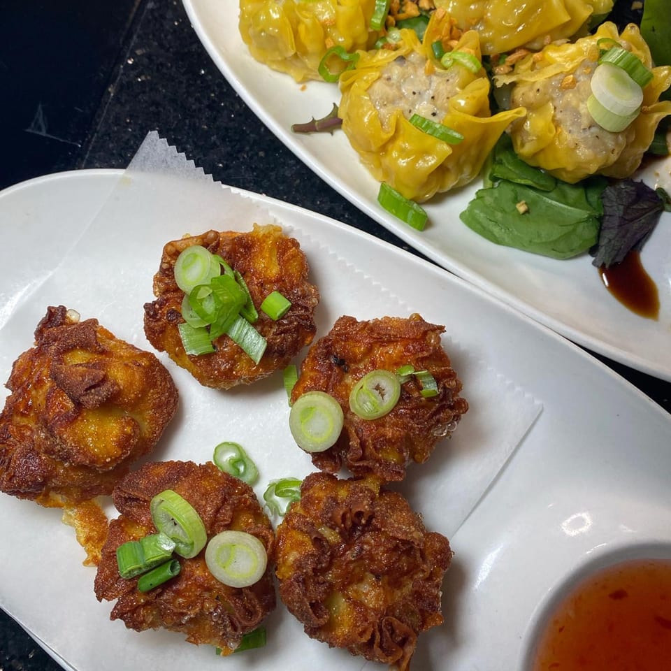 Crispy fried Thai shrimp cakes and steamed dumplings garnished with green onions on white plates.