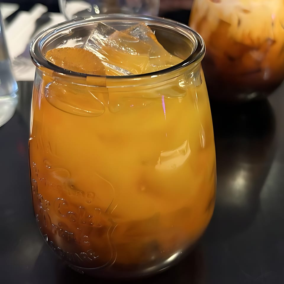 Iced Thai tea in a glass jar, with another drink blurred in the background.