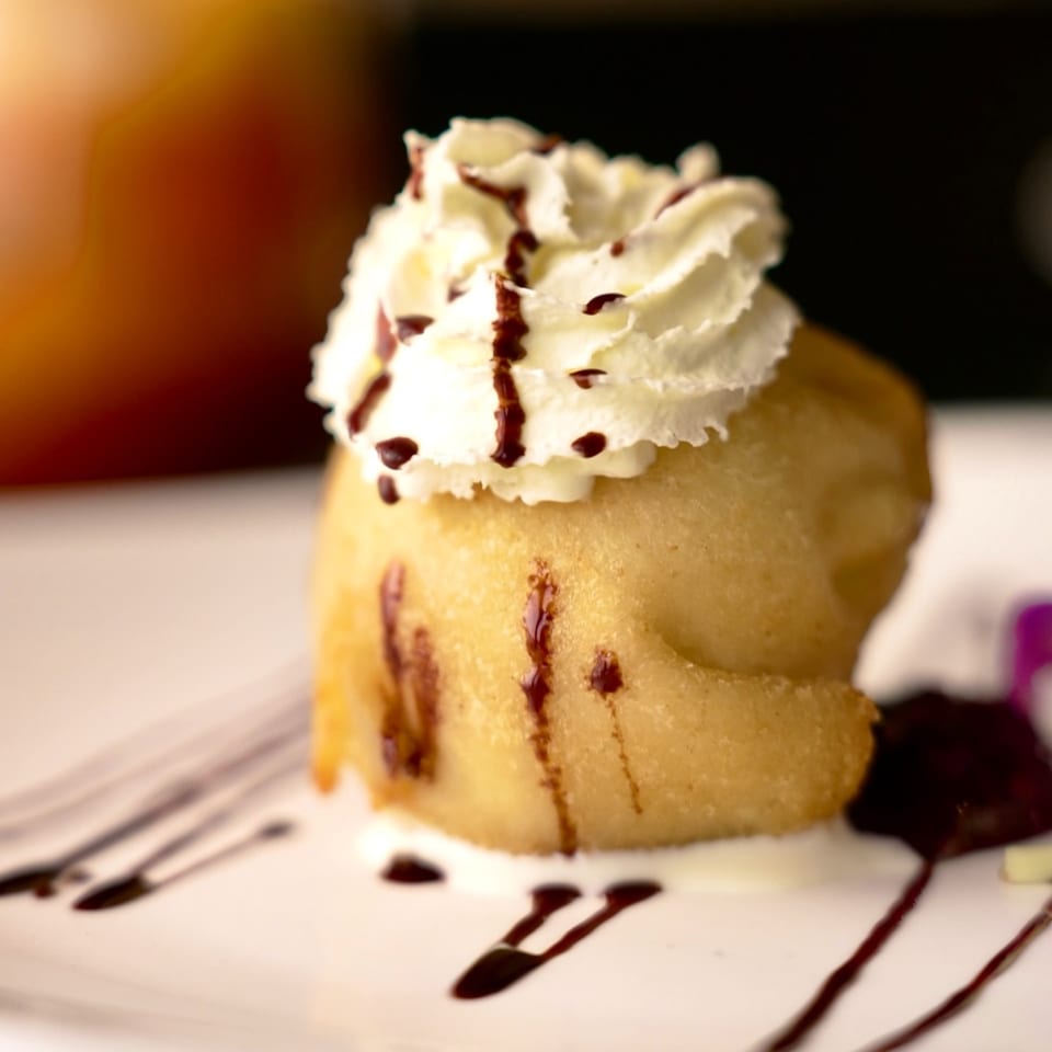 Fried banana dessert topped with whipped cream and chocolate syrup on a white plate.