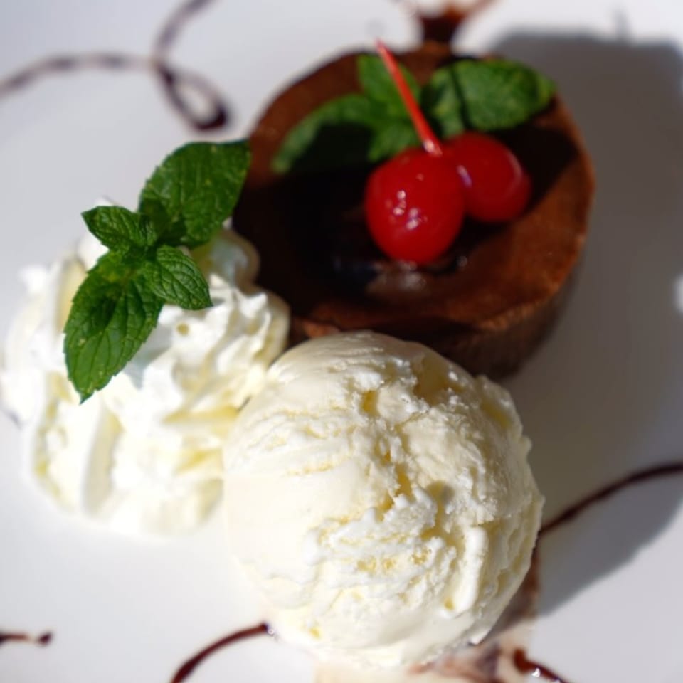 Chocolate lava cake with cherries, mint, whipped cream, and vanilla ice cream on a white plate.