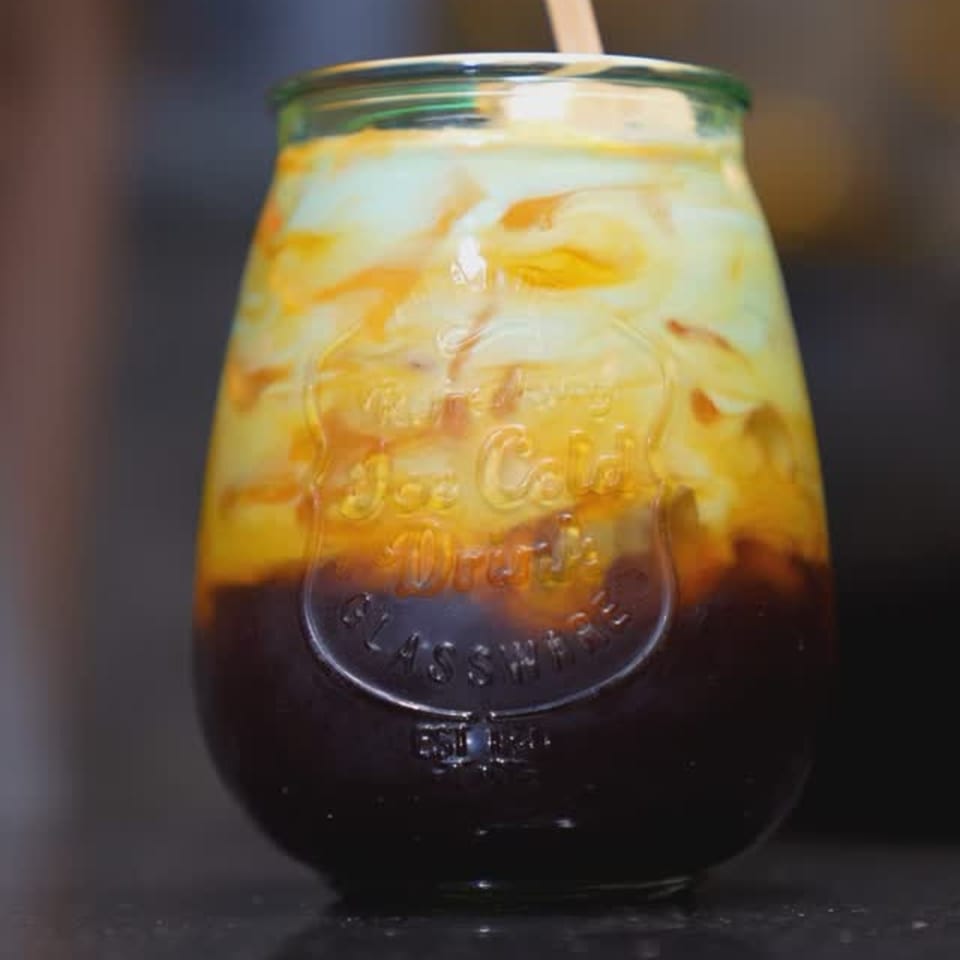 A glass of Thai iced tea with a straw, showing distinct layers of dark tea and creamy milk.