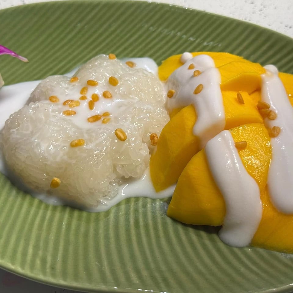 Mango sticky rice dessert with coconut milk and golden crispy beans on a green plate.