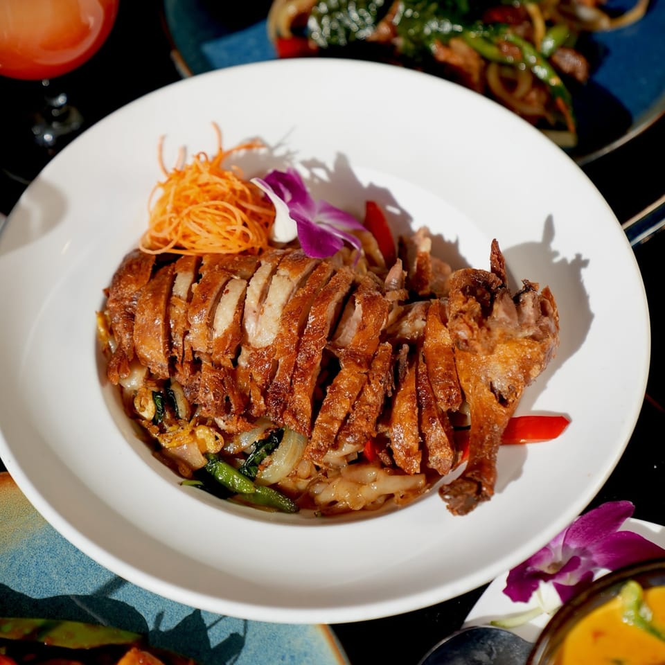 Crispy duck, sliced and served over noodles with vegetables, garnished with shredded carrots and an orchid.