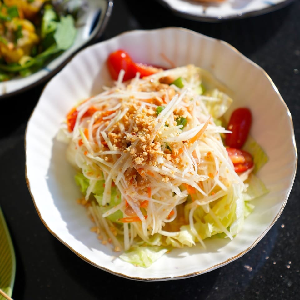 A white bowl of Maya Thai Eatery's papaya salad with shredded papaya, tomatoes, and crushed peanuts.